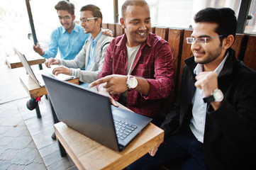 Fototapeta premium Group of four indian teen male students. Classmates spend time together and work at laptops.