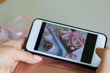 Girl takes on a smartphone airy pink marshmallows from cherries. Marshmallows decorated with chocolate.