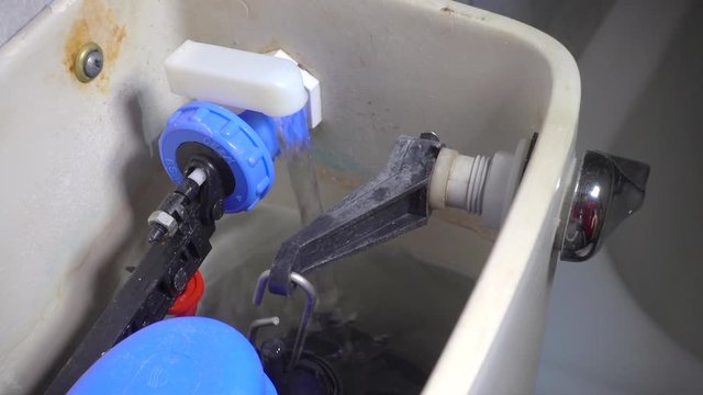 Slow motion close POV shot of a male plumber&rsquo;s hands adjusting the float valve for the water level in a toilet cistern, then flushing to test, with water flowing in as it refills.