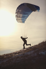 Silhouette of an athlete running down the hillside under the filled with a canopy of parachute before the flight. Speed flying.