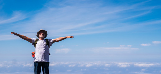 Active senior man standing and enjoying the top of the world opening arms and smiling - blue sky with clouds in background - concept of no limit age and travel for  old people