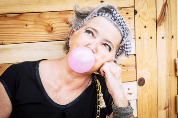 Alternative unusual pretty senior caucasian lady with trendy make up and grey hair blowing a pink...