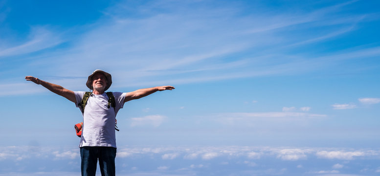 Active senior man standing and enjoying the top of the world opening arms and smiling - blue sky with clouds in background - concept of no limit age and travel for  old people
