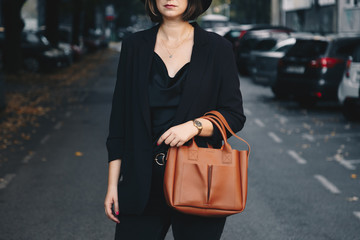 street style portrait of an attractive woman wearing black denim jeans, satin top, blazer, gold...
