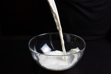А man pours milk into a glass Bowl to prepare pancakes. Also for drinking.