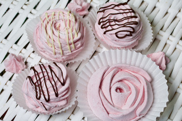 Aerial pink cherry marshmallows. Some in the shape of a rose, another decorated with chocolate. Against the background of wicker vines.