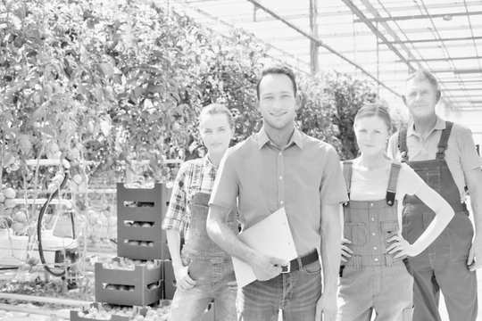 Black and white photo of Confident supervisor standing with farmers in greenhouse 