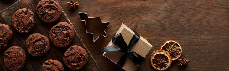 top view of chocolate Christmas cookies near gift box on wooden table, panoramic shot