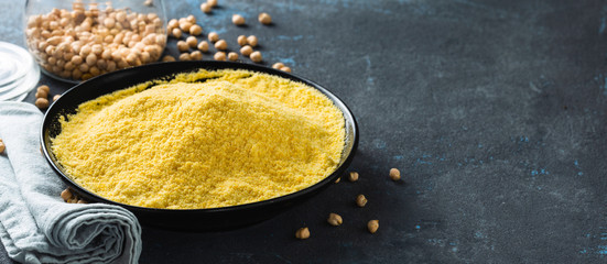 Chickpea flour in black ceramic bowl on dark background copy space