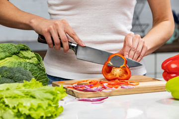 Close up of woman's hands cooking in the kitchen. Housewife slicing fresh Bell pepper. Vegetarian and healthily cooking concept