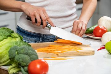 Close up of woman's hands cooking in the kitchen. Housewife slicing fresh carrot. Vegetarian and...