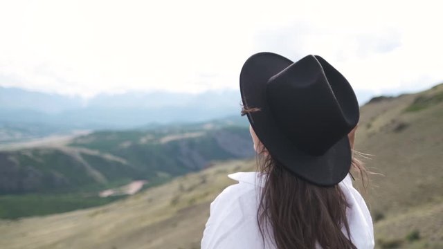 Attractive brunette in a hat and white shirt is enjoying nature in the mountains. portrait of a young woman in a hat on a background of a beautiful landscape.