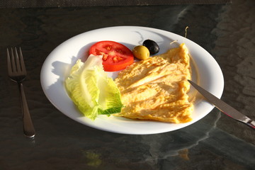 Close-up of a delicious egg omelet, salad, tomatoes, olives on a glass table in one white plate.A nutritious Breakfast illuminated by the morning light.The balance of protein and vitamins diet gourmet
