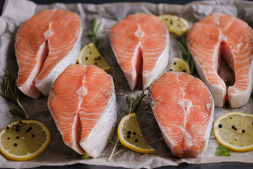 Raw, fresh salmon steaks on a baking tray with lemon, rosemary and cherry tomatoes. Raw salmon, red fish. Cooking salmon, seafood. Healthy eating concept. Salmon and spices