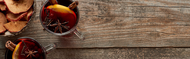 panoramic shot of red spiced mulled wine with berries, anise, orange slices and cinnamon on wooden rustic table