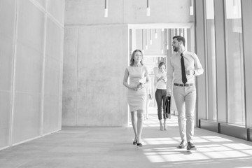 Black and white photo of business people discussing plans before meeting while walking in office hall