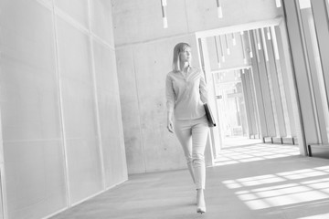 Black and white photo of businesswoman walking while holding document in office hall