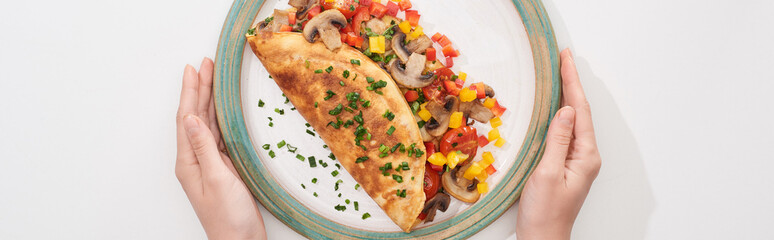 cropped view of woman holding plate with homemade wrapped omelet with vegetables