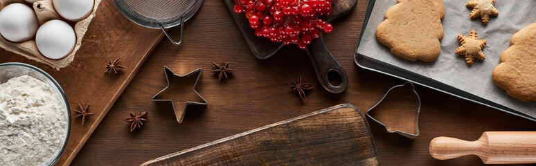 top view of baked Christmas cookies near ingredients, dough molds and viburnum on wooden table, panoramic shot
