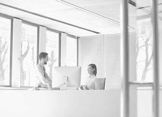 Black and white photo of businessman sitting on table while talking to receptionist in office lobby during break