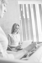 Black and white photo of businesswomen working while waiting in office lobby