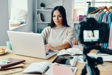 Fototapeta premium Beautiful young woman in casual clothing making social media video while using laptop at home