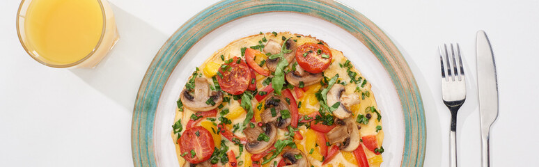 top view of plate with yummy omelet for breakfast on white table with glass of juice, fork and knife
