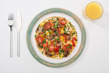 top view of tasty omelet for breakfast on white table with juice, fork and knife