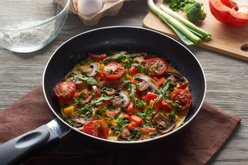 delicious homemade omelet in frying pan with ingredients on table
