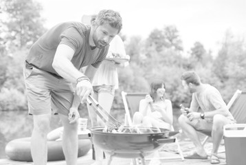 Man using bellows for preparing food in barbecue grill with friends on pier