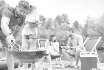 Man using bellows for preparing food in barbecue grill with friends on pier