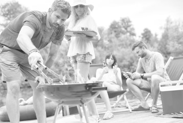 Man using bellows for preparing food in barbecue grill with friends on pier