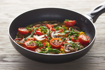 delicious homemade omelet with vegetables and greens in frying pan on wooden table
