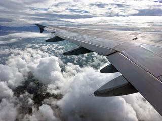 Viajando. Ala de un avión entre las nubes con las montañas al fondo.