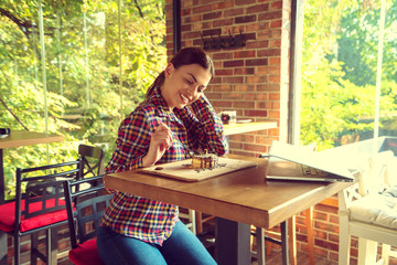 Fototapeta na wymiar Attractive happy young woman sitting and eating dessert in cafe