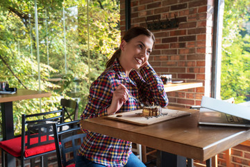 Attractive happy young woman sitting and eating dessert in cafe