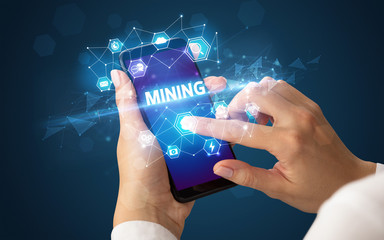Female hand holding smartphone with MINING inscription, modern technology concept