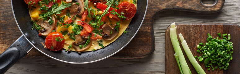 top view of delicious omelet in frying pan with fresh leek on wooden boards