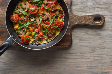 top view of homemade omelet in frying pan on wooden board