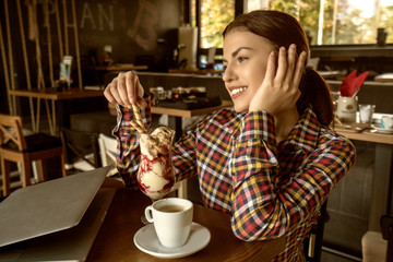 Attractive happy young woman sitting and eating dessert in cafe