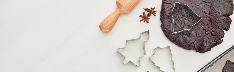 top view of raw dough for chocolate Christmas cookies near rolling pin and dough molds on white background, panoramic shot