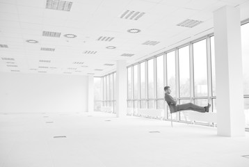 Full length of thoughtful young businessman sitting on chair while looking through window at new empty office