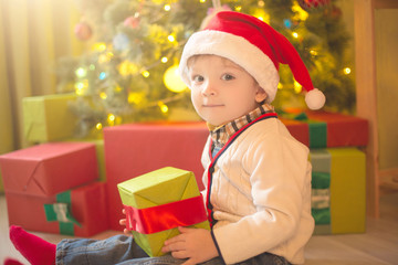 Happy little boy with Xmas present on Christmas Eve in decorated room. Sunny morning or day. Christmas or New Year holiday