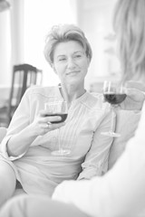 Mature women drinking wine while sitting in sofa at home