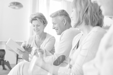 Fototapeta premium Smiling mature man holding digital tablet while sitting with friends at home