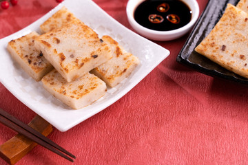 Chinese lunar new year food concept, Delicious turnip radish cake, local cuisine in restaurant with soy sauce on red background, close up, copy space