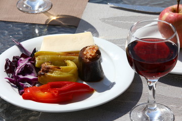 Stewed yellow and red peppers, stuffed eggplant, lilac cabbage and a slice of hard cheese in one plate on a glass table.Colorful vegetarian dinner with red wine in the restaurant.Selective focus