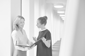 Fototapeta premium Black and white photo of Businesswomen discussing over document while standing in corridor at office