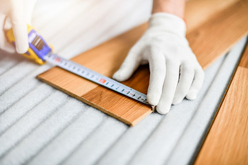 Close up of wood worker with in white gloves measuring tape and new laminated wooden floor board.