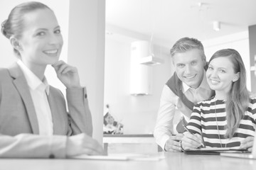 Black and white photo of Happy couple with relator signing a contract at table in apartment